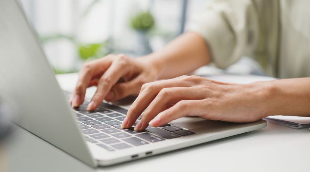 노트북 키보드 위에서 손으로 타이핑하며 온라인 정보를 확인하는 장면